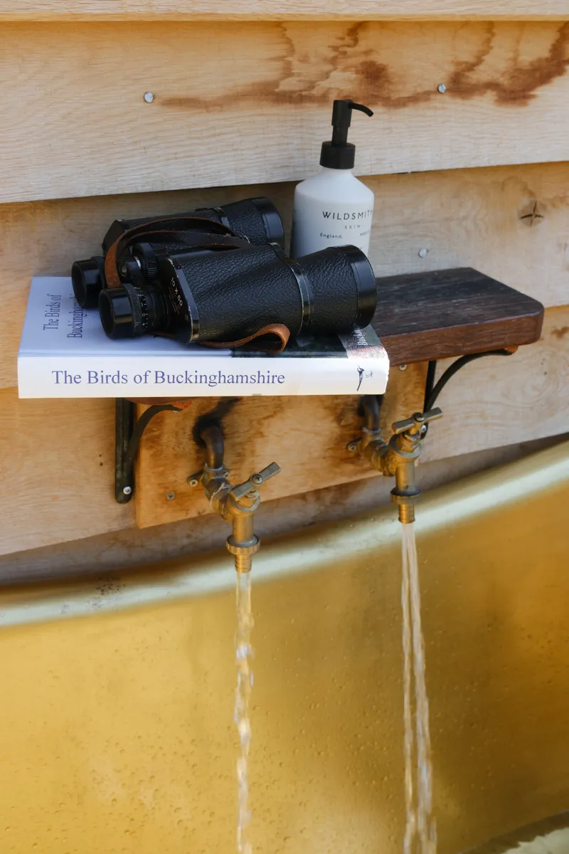 Binoculars on a copy of The Birds of Buckinghamshire, on a shelf above two outdoor taps